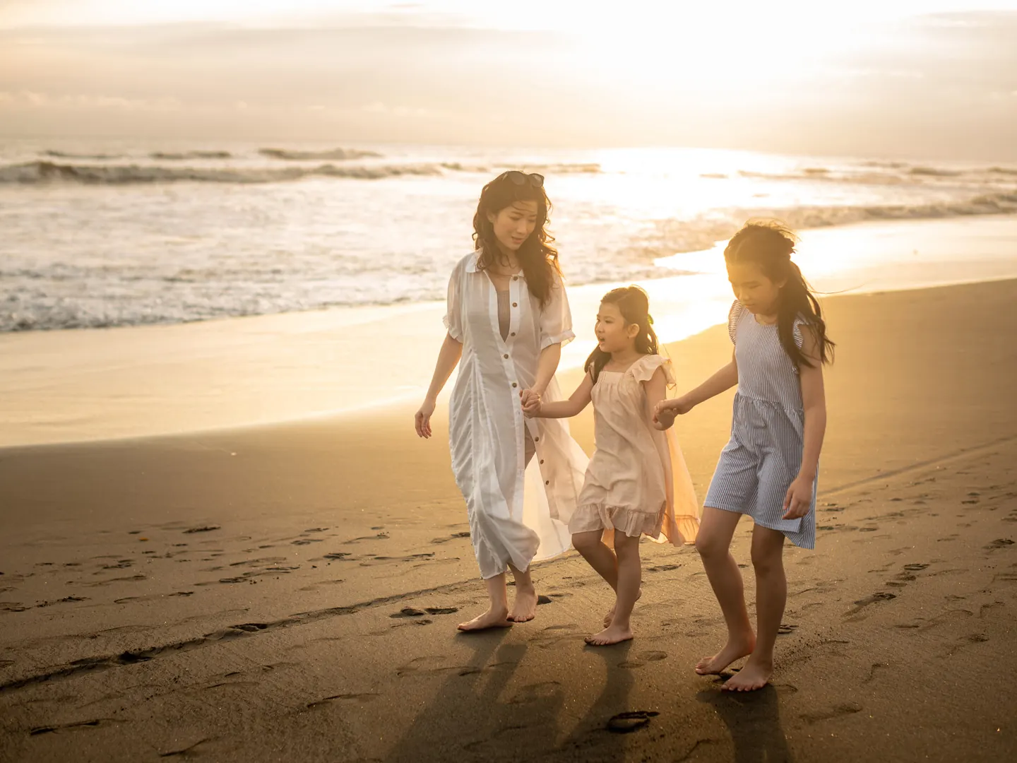 Mother and two daughters walking together on a Bali beach at sunset
